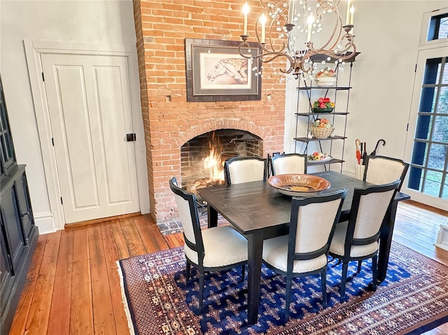 dining room with light wood-type flooring, a notable chandelier, and a brick fireplace