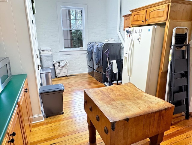 kitchen with white refrigerator with ice dispenser, washer and clothes dryer, and light hardwood / wood-style floors