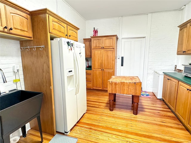 kitchen featuring light hardwood / wood-style floors, brick wall, sink, and white refrigerator with ice dispenser