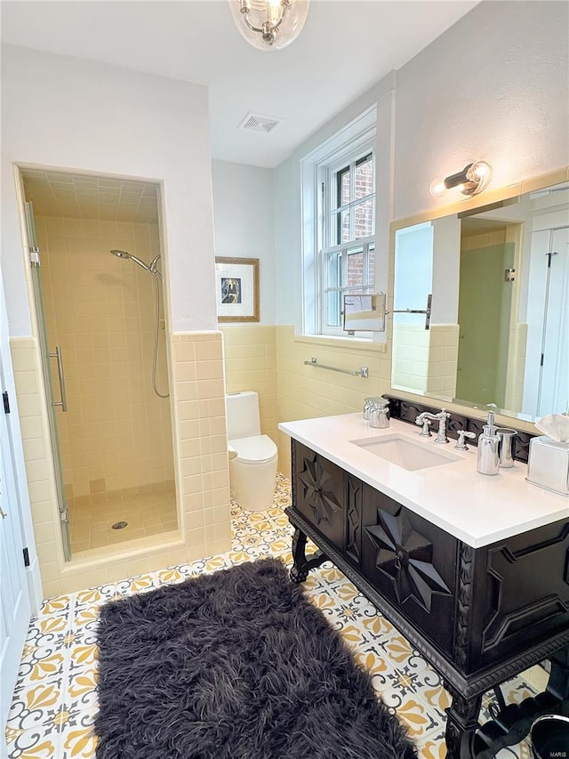 bathroom with a shower with door, vanity, tile patterned flooring, tile walls, and toilet