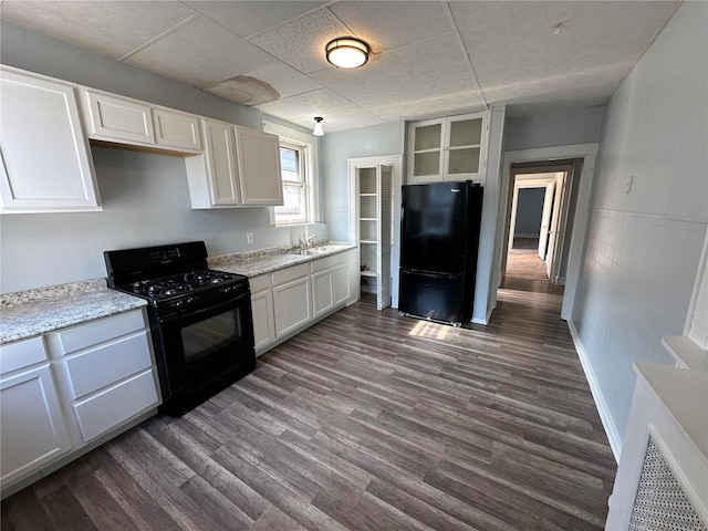 kitchen with white cabinets, light stone counters, sink, black appliances, and dark wood-type flooring