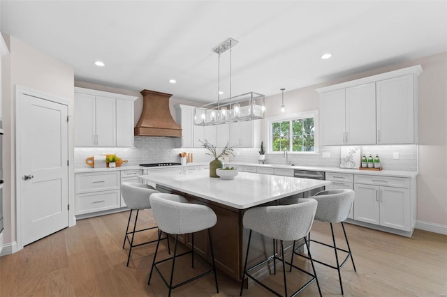 kitchen featuring white cabinets, a kitchen island, custom exhaust hood, and light hardwood / wood-style floors