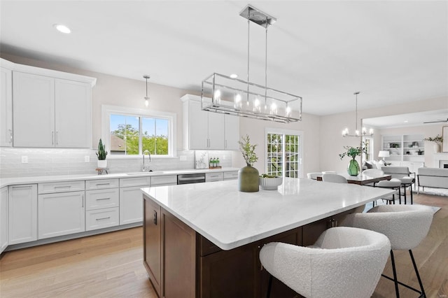 kitchen with light wood-type flooring, pendant lighting, white cabinetry, and sink