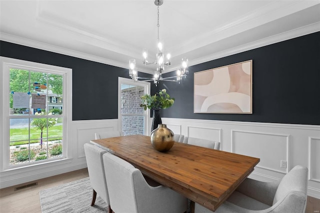 dining space featuring a tray ceiling, crown molding, a notable chandelier, and light hardwood / wood-style floors