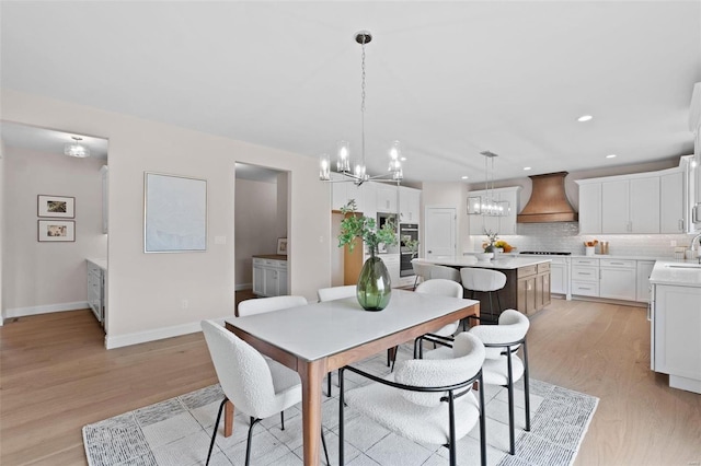 dining room with light wood-type flooring, a notable chandelier, and sink