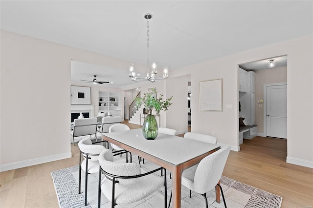 dining space with built in shelves, ceiling fan with notable chandelier, and light hardwood / wood-style floors