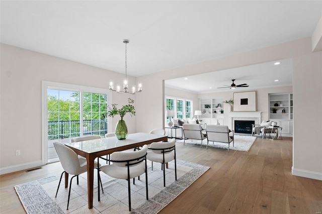 dining room featuring light wood-type flooring, ceiling fan with notable chandelier, a healthy amount of sunlight, and built in features