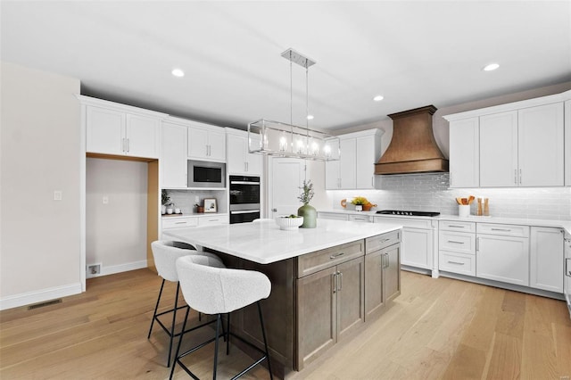 kitchen with custom range hood, appliances with stainless steel finishes, light hardwood / wood-style floors, white cabinetry, and a kitchen island