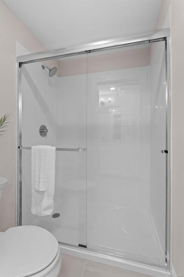 bathroom featuring toilet, a shower with shower door, and tile patterned flooring