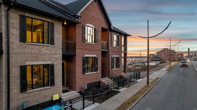 property exterior at dusk featuring entry steps, brick siding, and a fenced front yard