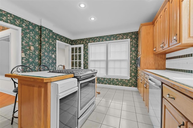 kitchen featuring baseboards, wallpapered walls, stainless steel appliances, a breakfast bar area, and light tile patterned floors