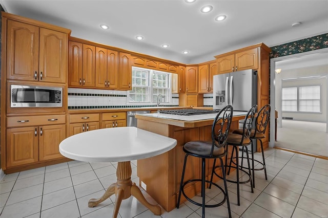 kitchen featuring light countertops, a sink, a center island, light tile patterned floors, and stainless steel appliances