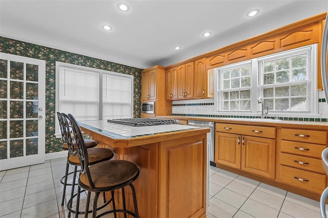 kitchen with appliances with stainless steel finishes, sink, light tile patterned floors, a center island, and tile counters