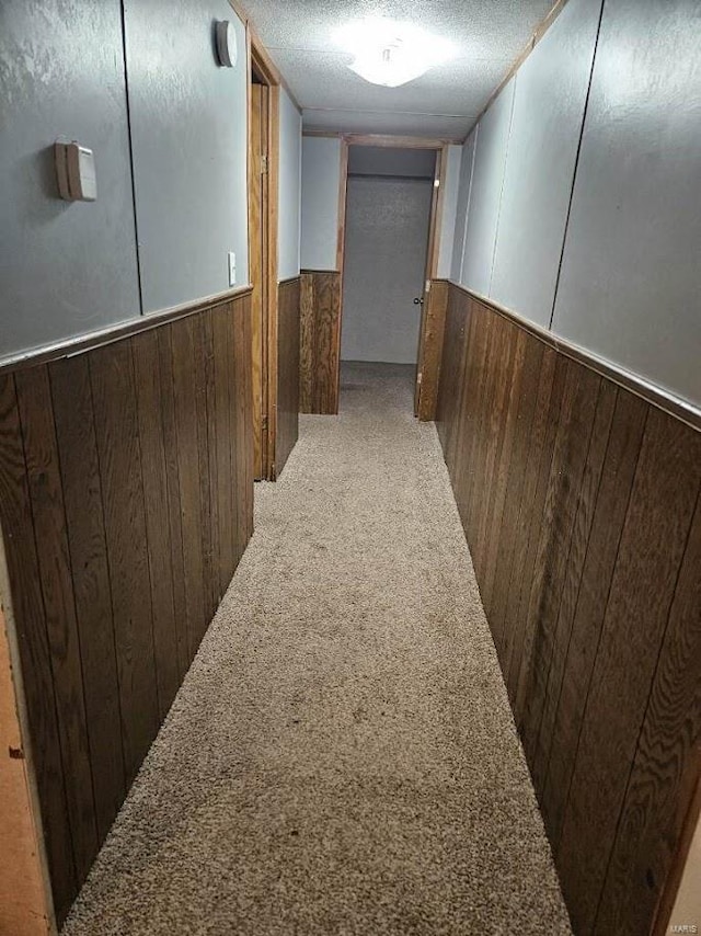 hallway featuring a textured ceiling, carpet, and wood walls