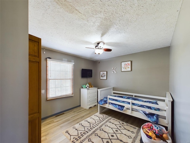 bedroom with light wood-type flooring, ceiling fan, and a textured ceiling