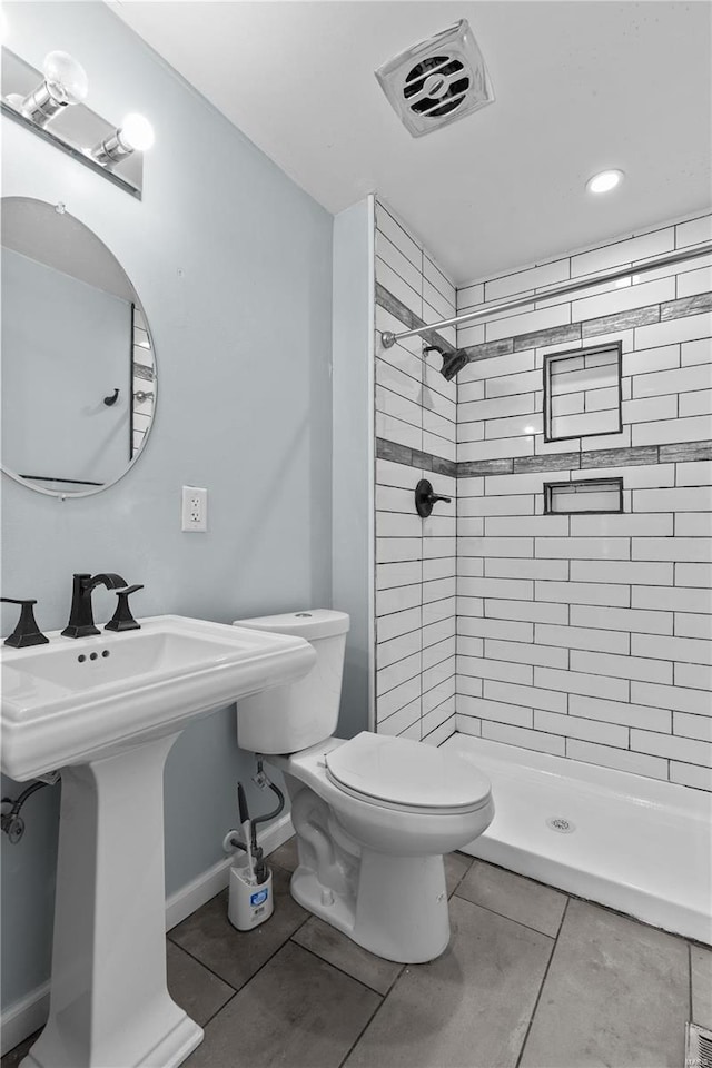 bathroom featuring a tile shower, toilet, and tile patterned flooring