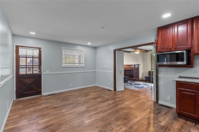 kitchen featuring a brick fireplace, stainless steel microwave, dark hardwood / wood-style floors, and ceiling fan