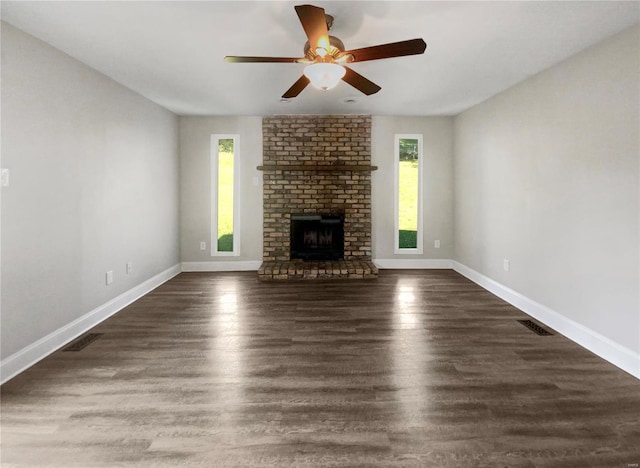 unfurnished living room featuring dark wood-type flooring, a brick fireplace, brick wall, and ceiling fan