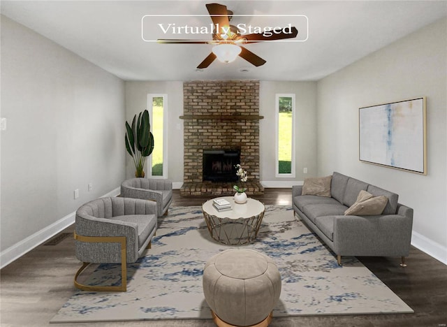 living room featuring dark wood-type flooring, ceiling fan, brick wall, and a brick fireplace