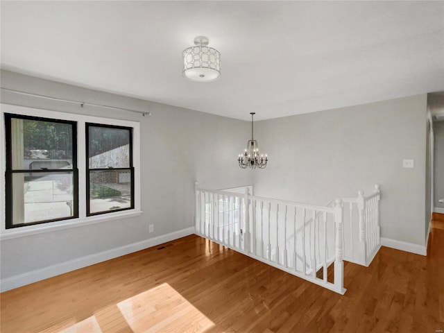 empty room featuring wood-type flooring and an inviting chandelier