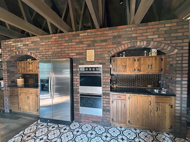 kitchen featuring double oven, stainless steel fridge with ice dispenser, sink, and beam ceiling