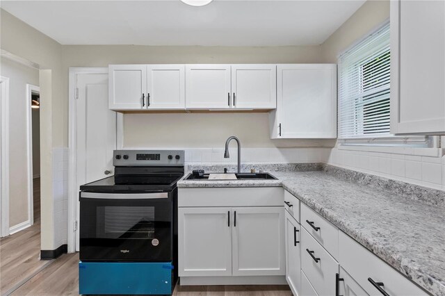 kitchen featuring stainless steel electric range, sink, white cabinets, and light hardwood / wood-style floors