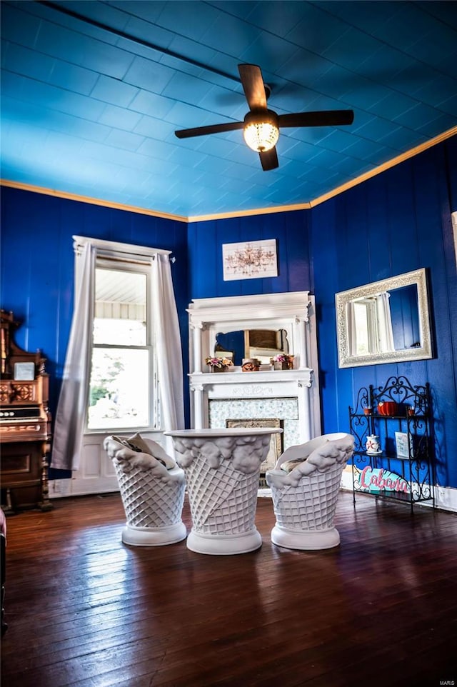 living room with dark wood-type flooring, ceiling fan, ornamental molding, and a fireplace