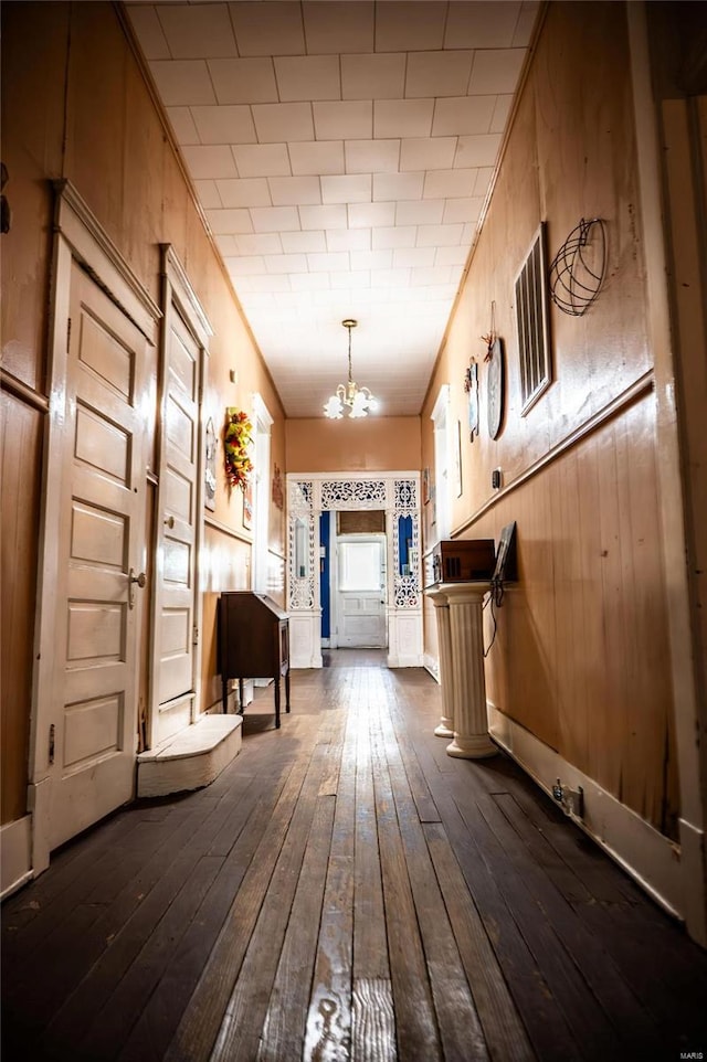 mudroom with dark wood-type flooring, a notable chandelier, and wooden walls