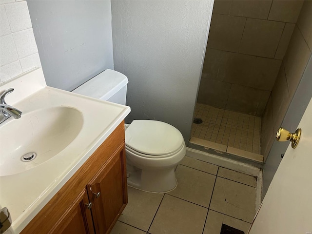 bathroom with tiled shower, tile patterned flooring, toilet, and vanity