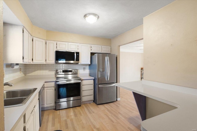 kitchen featuring light wood-style flooring, a sink, light countertops, appliances with stainless steel finishes, and backsplash