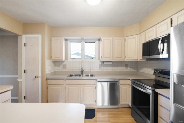 kitchen featuring light wood-type flooring, a sink, stainless steel appliances, light countertops, and decorative backsplash