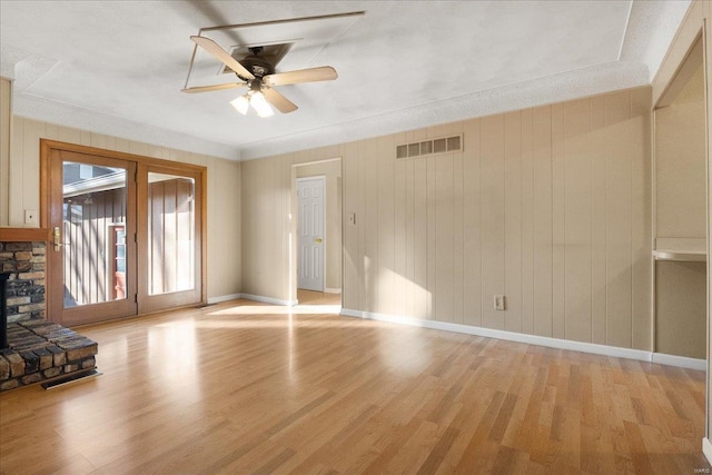 unfurnished living room featuring visible vents, baseboards, a stone fireplace, light wood-style flooring, and a ceiling fan