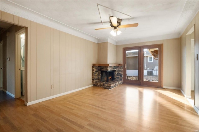 unfurnished living room featuring light wood finished floors, a stone fireplace, baseboards, and ceiling fan