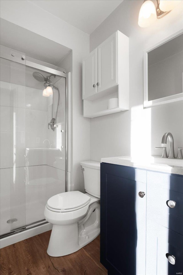 bathroom featuring a stall shower, toilet, vanity, and wood finished floors