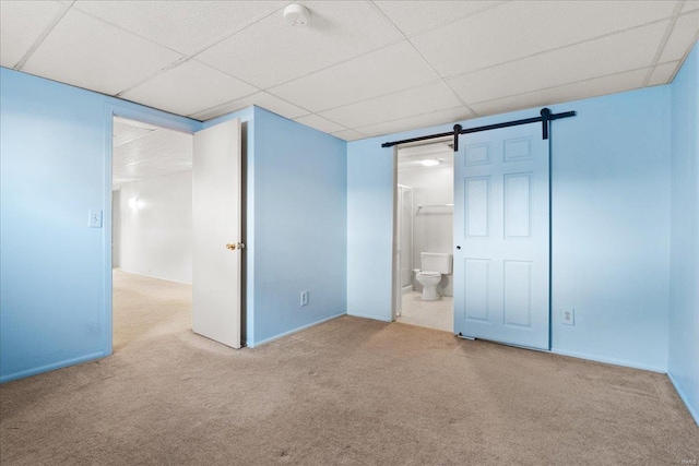 unfurnished bedroom with baseboards, a barn door, carpet floors, ensuite bathroom, and a paneled ceiling