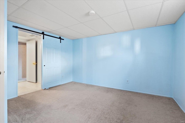 unfurnished room with a drop ceiling, a barn door, and carpet floors