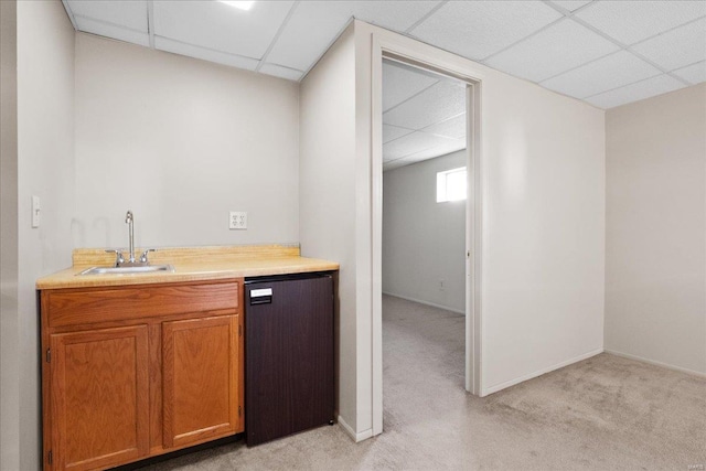 bar featuring baseboards, a drop ceiling, light colored carpet, dishwashing machine, and a sink