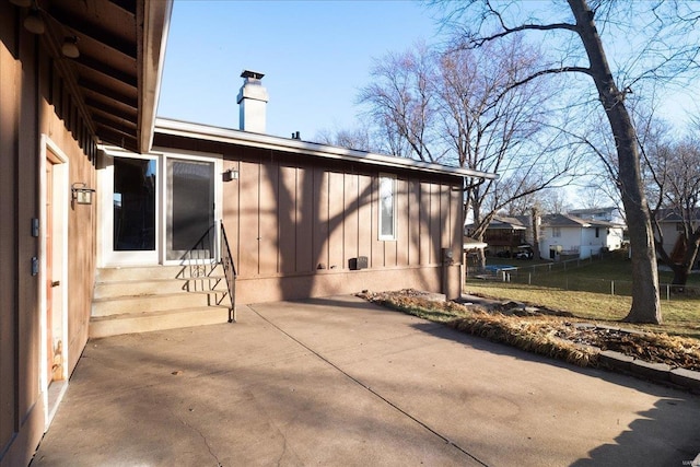 view of property exterior with board and batten siding, fence, entry steps, a chimney, and a patio area