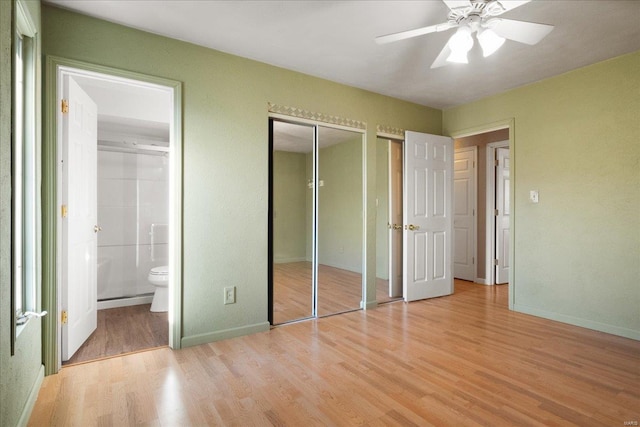 unfurnished bedroom featuring a ceiling fan, baseboards, multiple closets, light wood-type flooring, and connected bathroom