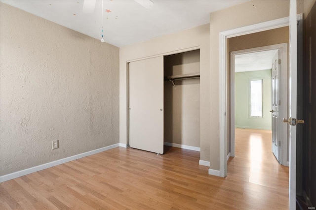 unfurnished bedroom with a closet, baseboards, light wood-style floors, and a textured wall