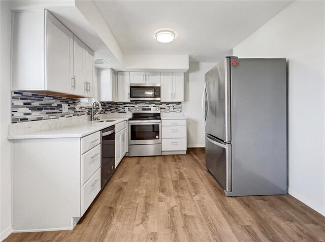 kitchen with white cabinets, stainless steel appliances, decorative backsplash, and light hardwood / wood-style flooring