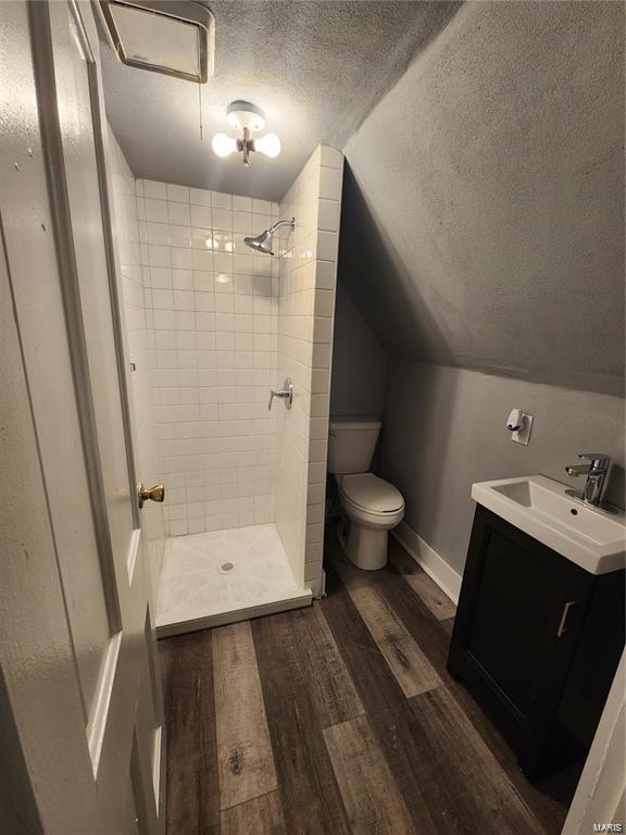 bathroom with hardwood / wood-style floors, toilet, a tile shower, and vanity