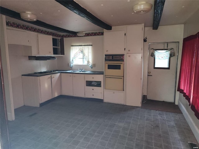 kitchen featuring beamed ceiling, white cabinetry, wall oven, and sink