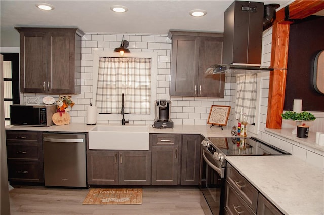 kitchen with wall chimney range hood, appliances with stainless steel finishes, backsplash, sink, and light hardwood / wood-style flooring