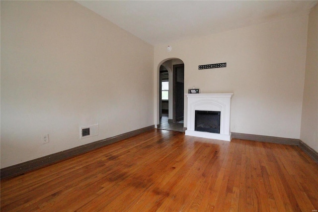 unfurnished living room featuring baseboards, visible vents, arched walkways, hardwood / wood-style floors, and a fireplace