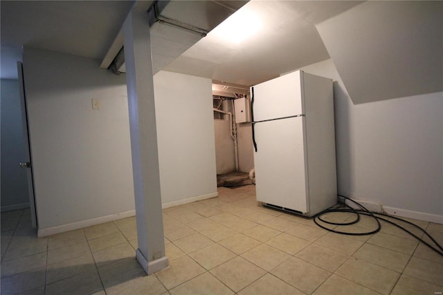 finished basement with light tile patterned flooring, freestanding refrigerator, and baseboards