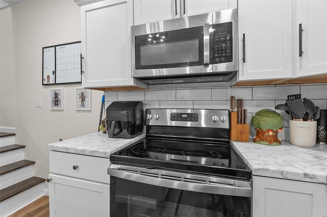 kitchen featuring backsplash, wood-type flooring, stainless steel appliances, and white cabinets