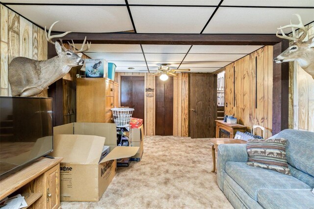 basement featuring a paneled ceiling, carpet, wooden walls, and ceiling fan