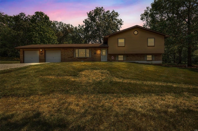 tri-level home featuring a yard, brick siding, gravel driveway, and an attached garage