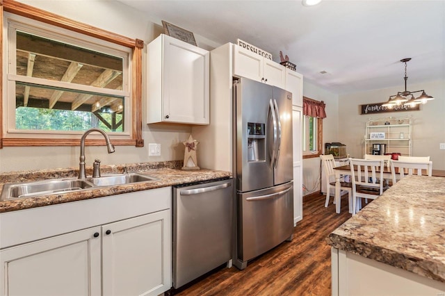 kitchen featuring dark wood-style floors, a sink, stainless steel appliances, white cabinets, and decorative light fixtures